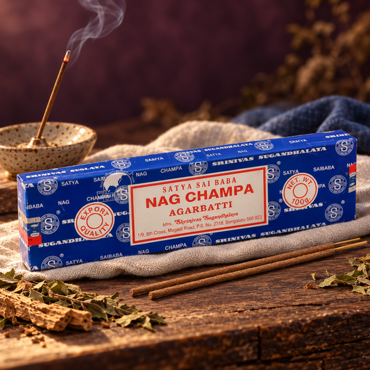 Incenso Satya Nag Champa com embalagem azul, ervas decorativas e incensário de cerâmica sobre linho claro.